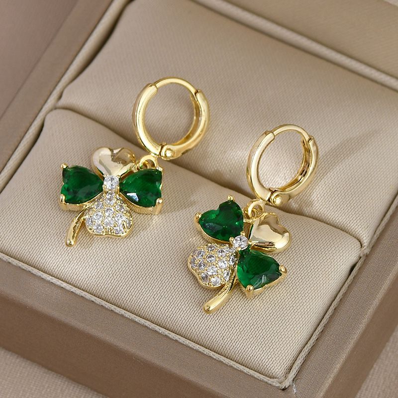 Gold shamrock earrings with green gemstones on a beige jewelry box