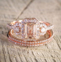 Rose gold ring with emerald-cut center stone and diamond accents on a textured surface