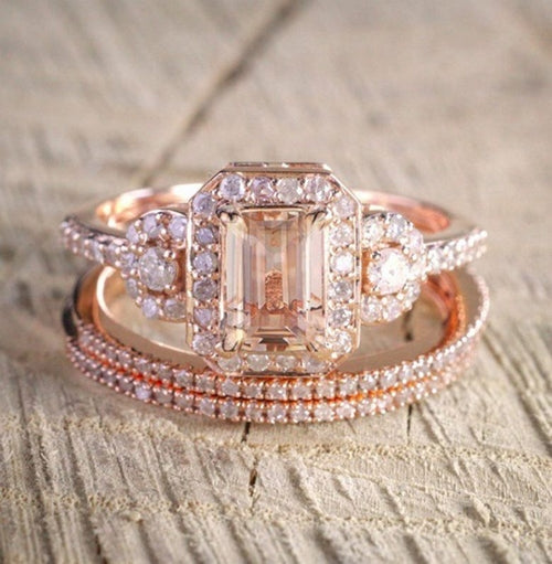 Rose gold ring with emerald-cut center stone and diamond accents on a textured surface