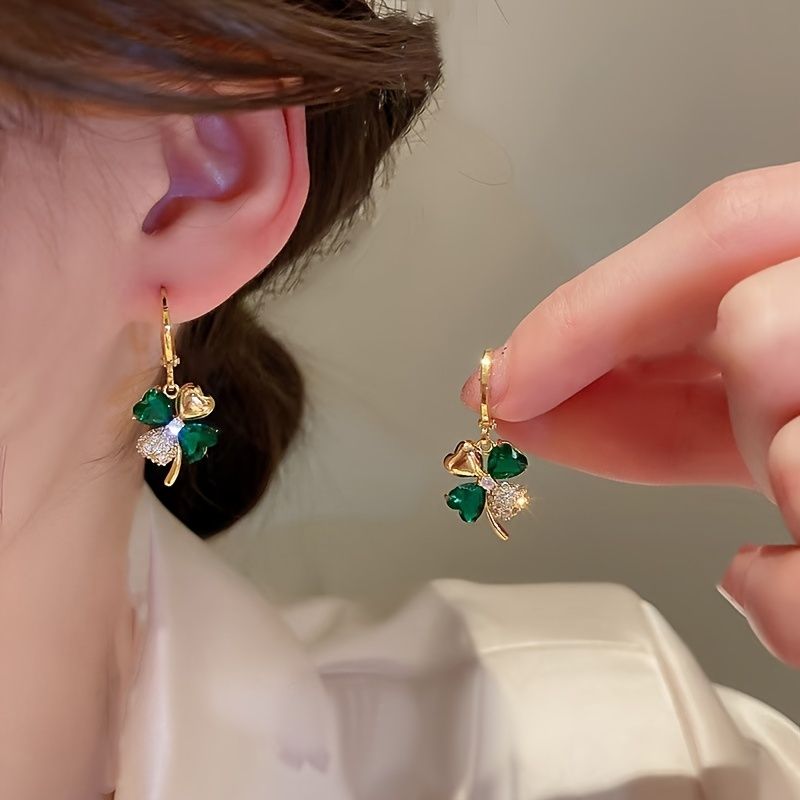 Close-up of a person wearing gold earrings with green gemstones.