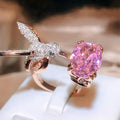 Rose gold ring with pink gemstone and intricate design on a white surface